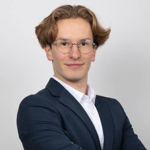 Professional headshot of Louan Bardou wearing glasses, a navy suit jacket, and white shirt against a light gray background.