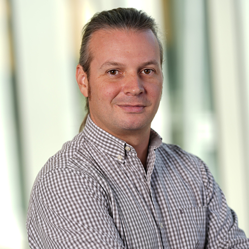 Headshot of Spyridon Bakas, PhD, wearing a checkered button-down shirt with his arms crossed, against a softly blurred light background.